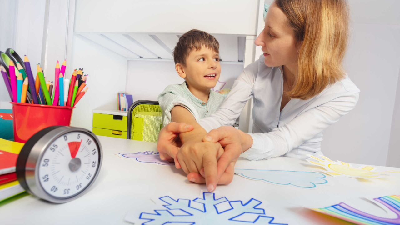 Boy with autism spectrum disorder learn weather using cards, teacher hold hands and point to correct one